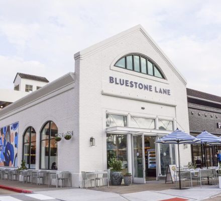Bluestone Lane cafe storefront with outdoor seating and blue umbrellas.
